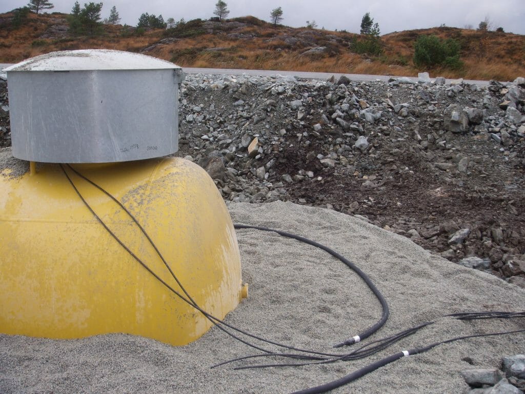 Yellow storage tank partly buried with cable-like polymer anode installed around the tank